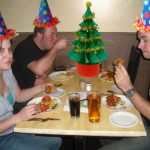 Christmas party with three silly party hats, people eating and a Christmas tree.