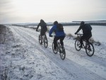 Three mountain bikers on snowy road.
