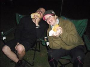 Two people stuffing their faces at a barbeque.