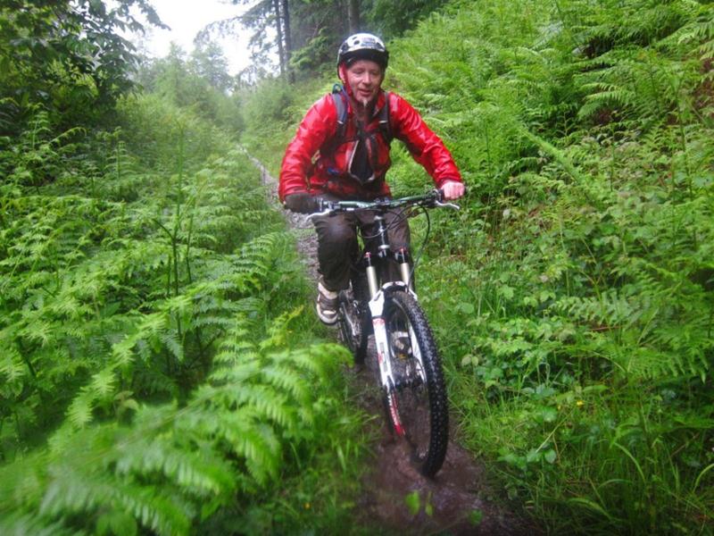 Wet mountain biker riding up a hill.