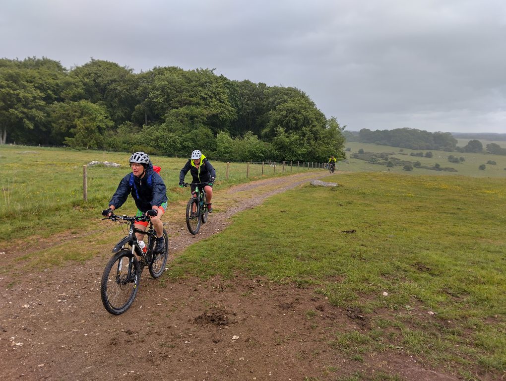 Mountain bikers riding on a gravel track in green countryside.